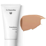 A white tube labeled Dr Hauschka Foundation 30ml is displayed next to a swatch of medium coverage natural foundation cream on a white background.