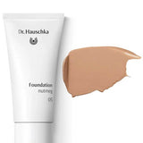 A white tube labeled Dr Hauschka Foundation 30ml is displayed next to a swatch of medium coverage natural foundation cream on a white background.