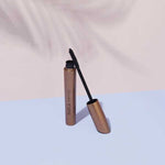 INIKA Organic Curvy Lash Mascara tube and curved black wand arranged on pastel blue and blush pink surfaces.