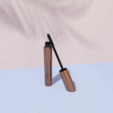 INIKA Organic Curvy Lash Mascara tube and curved black wand arranged on pastel blue and blush pink surfaces.