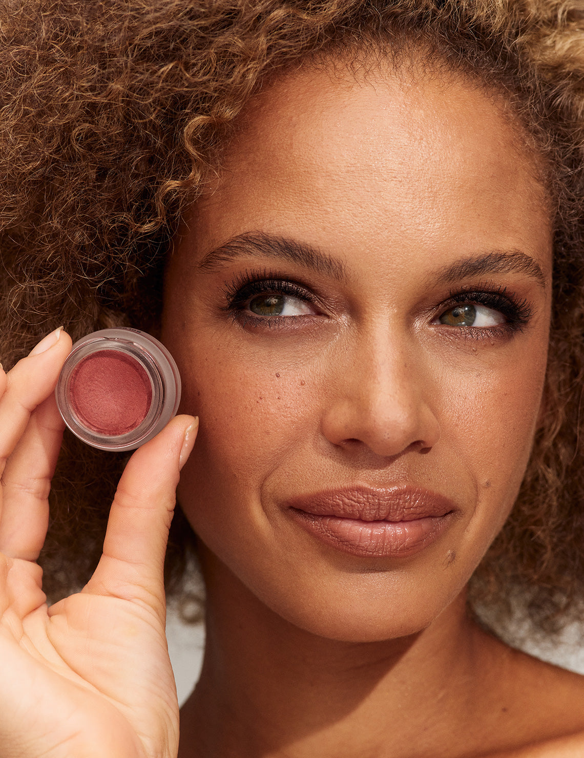 Model wearing and holding INIKA Organic Lip and Cheek Cream