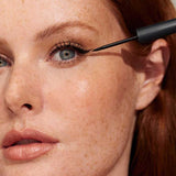 Close-up of a freckled model applying black INIKA Organic Liquid Eyeliner precisely along the upper lash line.