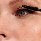 Close-up of a model applying INIKA Organic Long Lash Mascara to the upper lashes, showing the brush and defined eye.
