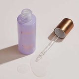 Open lavender INIKA Organic Bakuchiol Serum bottle and gold dropper arranged beside a pool of clear serum on a pale surface.