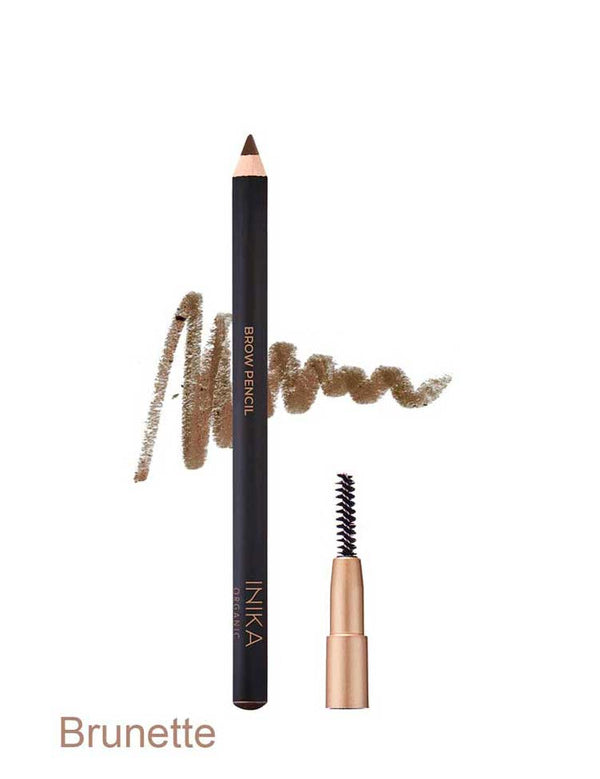 Black INIKA brow pencil in Brunette standing beside a small spoolie brush in a gold cap, with a medium brown scribbled swatch behind the pencil and the shade name Brunette printed below.