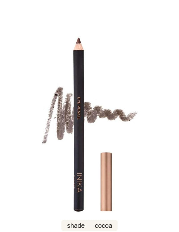 Black INIKA eyeliner pencil standing beside its bronze cap, with a brown scribbled colour swatch behind it. The caption identifies the shade as Cocoa.