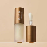 A frosted bottle of INIKA Organic Lip Oil - Collagen + Squalane Clear 5ml with a bronze cap is displayed; the cap stands beside the bottle, exposing a sponge-tip applicator. The backdrop features a soft beige tone.