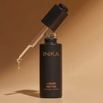 Open bottle of INIKA Organic Liquid Nectar Primer standing upright with the dropper suspended above and a bead of primer at its tip against a warm beige background.