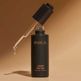 Open bottle of INIKA Organic Liquid Nectar Primer standing upright with the dropper suspended above and a bead of primer at its tip against a warm beige background.
