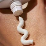 A close-up of a white tube of INIKA Organic Natural Sunscreen SPF50+ 50ml dispensing a wavy line onto a person’s skin.