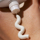 A close-up of a white tube of INIKA Organic Natural Sunscreen SPF50+ 50ml dispensing a wavy line onto a person’s skin.