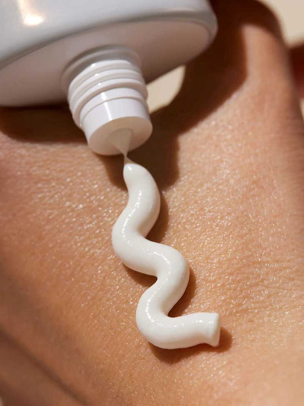 A close-up of a white tube of INIKA Organic Natural Sunscreen SPF50+ 50ml dispensing a wavy line onto a person’s skin.