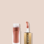 Open frosted INIKA tinted lip oil bottle containing peach-pink oil beside its upright sponge-tip applicator in a gold cap, on a beige background.