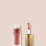 Open frosted INIKA tinted lip oil bottle containing peach-pink oil beside its upright sponge-tip applicator in a gold cap, on a beige background.