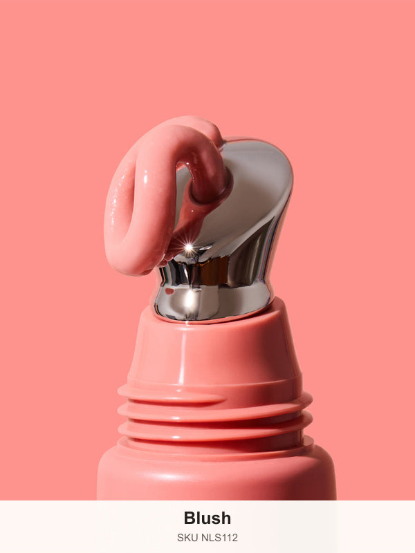 Thick glossy pink INIKA lip serum curling over the slanted silver applicator on a coral-pink tube against a matching background. The caption identifies the shade as Blush.