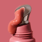 Thick glossy rose-pink INIKA lip serum curling down the slanted silver applicator on a dusty-pink tube against a matching background. The caption identifies the shade as Peony.