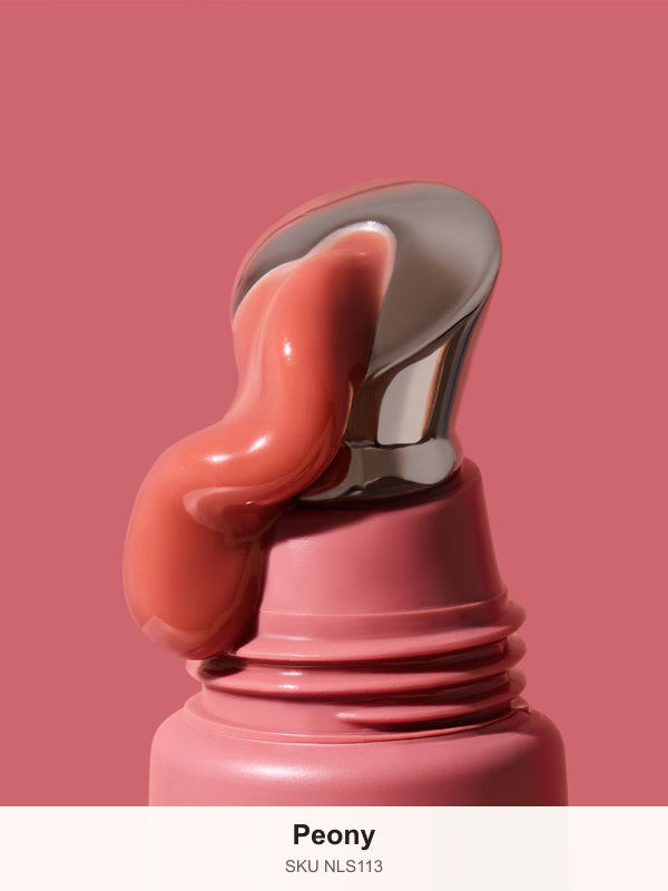 Thick glossy rose-pink INIKA lip serum curling down the slanted silver applicator on a dusty-pink tube against a matching background. The caption identifies the shade as Peony.