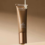 INIKA Organic Clear Tinted Lip Serum tube suspended against a warm brown studio background.