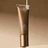 INIKA Organic Clear Tinted Lip Serum tube suspended against a warm brown studio background.