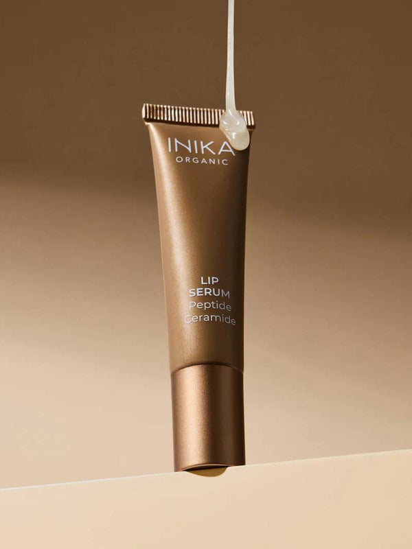 INIKA Organic Clear Tinted Lip Serum tube suspended against a warm brown studio background.