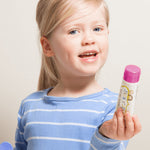 Smiling child holding Jack N' Jill Berries and Cream toothpaste and its purple cap against a bright white background.