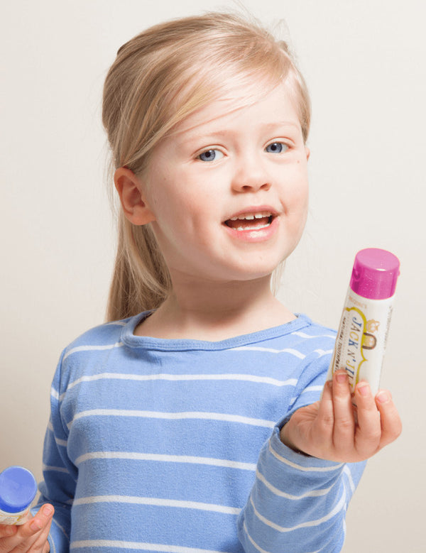 Smiling child holding Jack N' Jill Berries and Cream toothpaste and its purple cap against a bright white background.