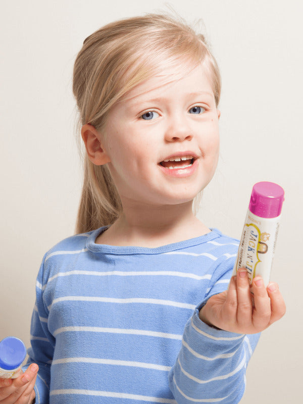Smiling child holding Jack N' Jill Berries and Cream toothpaste and its purple cap against a bright white background.