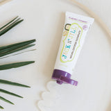 Open Jack N' Jill Blackcurrant toothpaste tube on a round white tray beside a palm frond and a wavy line of translucent paste.