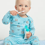 Young child in turquoise pyjamas brushing their teeth while holding an open Jack N' Jill Blueberry toothpaste tube.