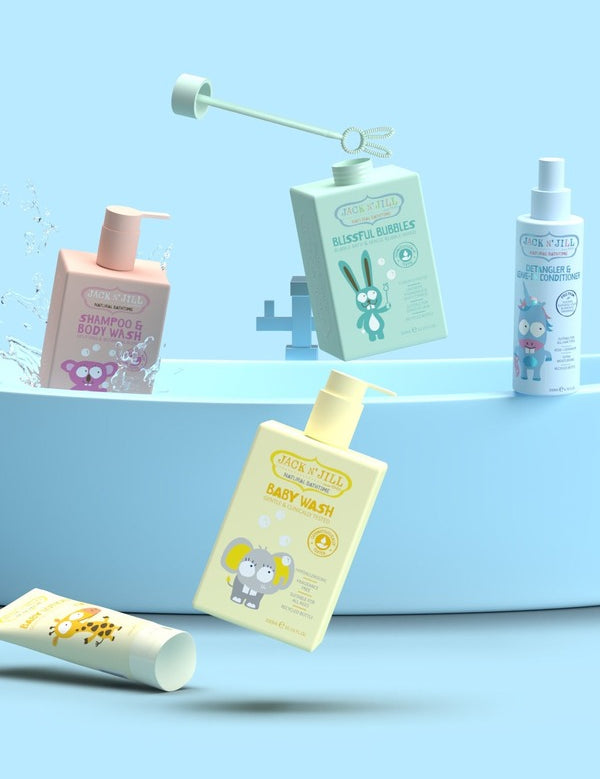 Colourful Jack N' Jill children's bath products arranged around a small blue bathtub, including baby wash, shampoo and body wash, bubble bath and spray.