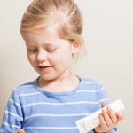 Child with blonde hair in a high bun holding a Jack N' Jill Flavour Free toothpaste tube while preparing to brush.