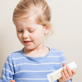 Child with blonde hair in a high bun holding a Jack N' Jill Flavour Free toothpaste tube while preparing to brush.