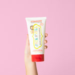Hand holding the large Jack N' Jill Mega Berry Strawberry toothpaste tube upright against a bright pink background.