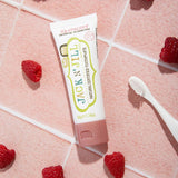 Jack N' Jill Raspberry toothpaste tube arranged on pink tiles with fresh raspberries and a white toothbrush.