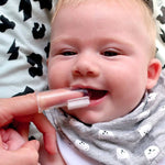 Smiling baby having their gums cleaned with the Jack N' Jill Stage 1 silicone finger brush while wearing a patterned bib.
