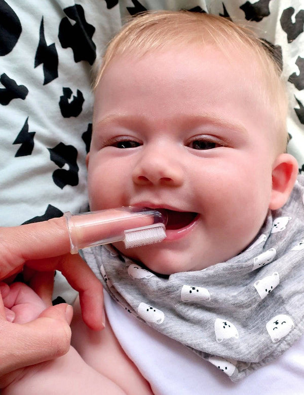 Smiling baby having their gums cleaned with the Jack N' Jill Stage 1 silicone finger brush while wearing a patterned bib.