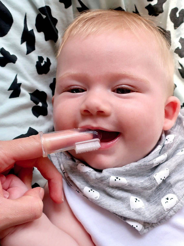 Smiling baby having their gums cleaned with the Jack N' Jill Stage 1 silicone finger brush while wearing a patterned bib.