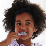 Young child brushing their teeth with the Jack N' Jill Stage 3 silicone tooth and gum brush, smiling against a bright white background.
