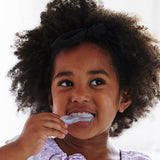 Young child brushing their teeth with the Jack N' Jill Stage 3 silicone tooth and gum brush, smiling against a bright white background.