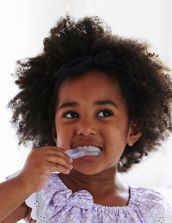 Young child brushing their teeth with the Jack N' Jill Stage 3 silicone tooth and gum brush, smiling against a bright white background.