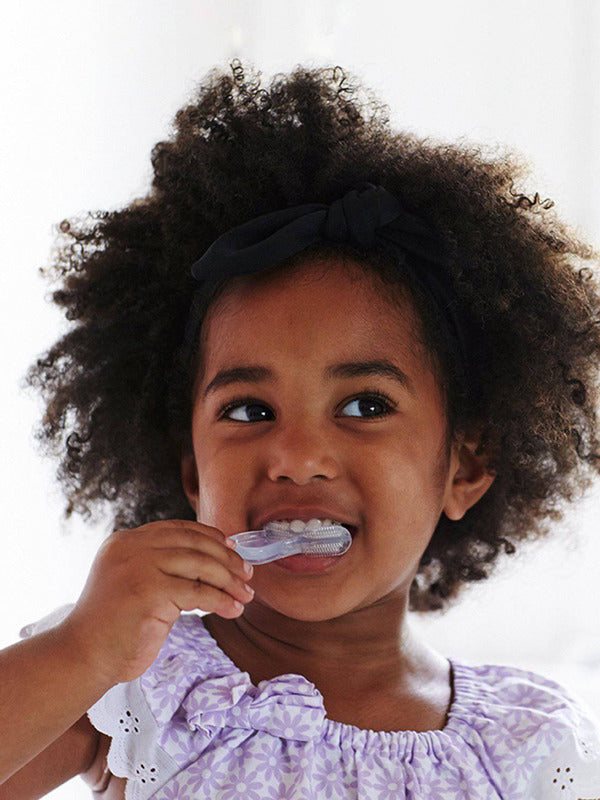 Young child brushing their teeth with the Jack N' Jill Stage 3 silicone tooth and gum brush, smiling against a bright white background.