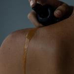 Juniper Anti Ageing Revitalising Body Oil being sprayed onto a shoulder in a close-up application shot.