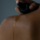 Juniper Anti Ageing Revitalising Body Oil being sprayed onto a shoulder in a close-up application shot.