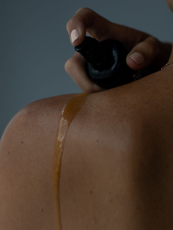 Juniper Anti Ageing Revitalising Body Oil being sprayed onto a shoulder in a close-up application shot.