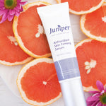 Juniper Antioxidant Skin Firming Serum tube styled among fresh grapefruit slices and pink flowers.