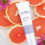 Juniper Antioxidant Skin Firming Serum tube styled among fresh grapefruit slices and pink flowers.