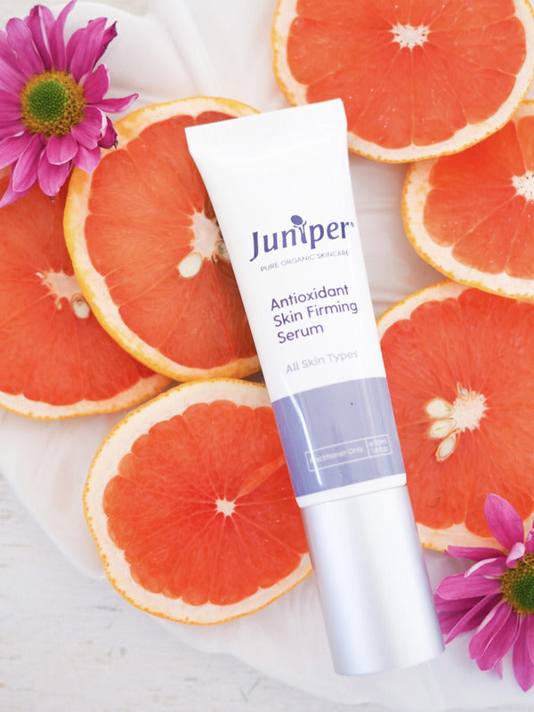 Juniper Antioxidant Skin Firming Serum tube styled among fresh grapefruit slices and pink flowers.