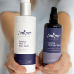Person holding Juniper Calming Face and Body Wash and Calming Treatment Serum forward with both labels visible.