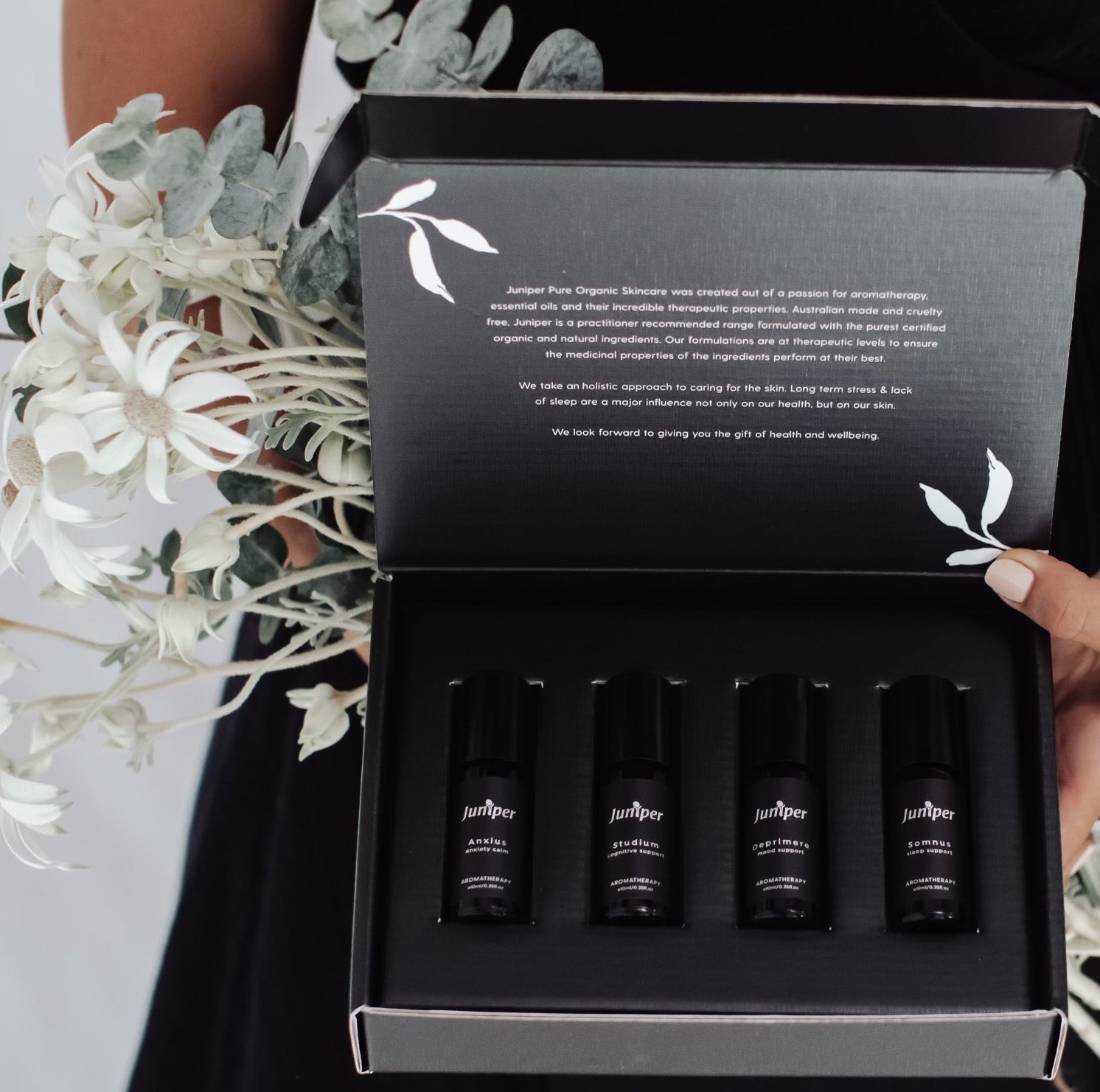 Juniper Cognitive Support and Wellbeing aromatherapy collection held open with flowers