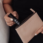 Juniper Deprimere 10ml aromatherapy roller, included in the Cognitive Support + Wellbeing Collection, held beside an open pink handbag.